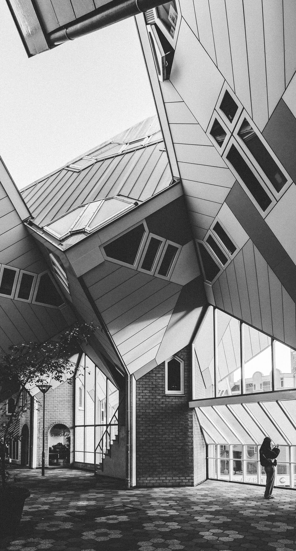 A black and white photograph of the incredible Cube Houses, designed by architect Piet Blom. A woman in the foreground takes a photograph.