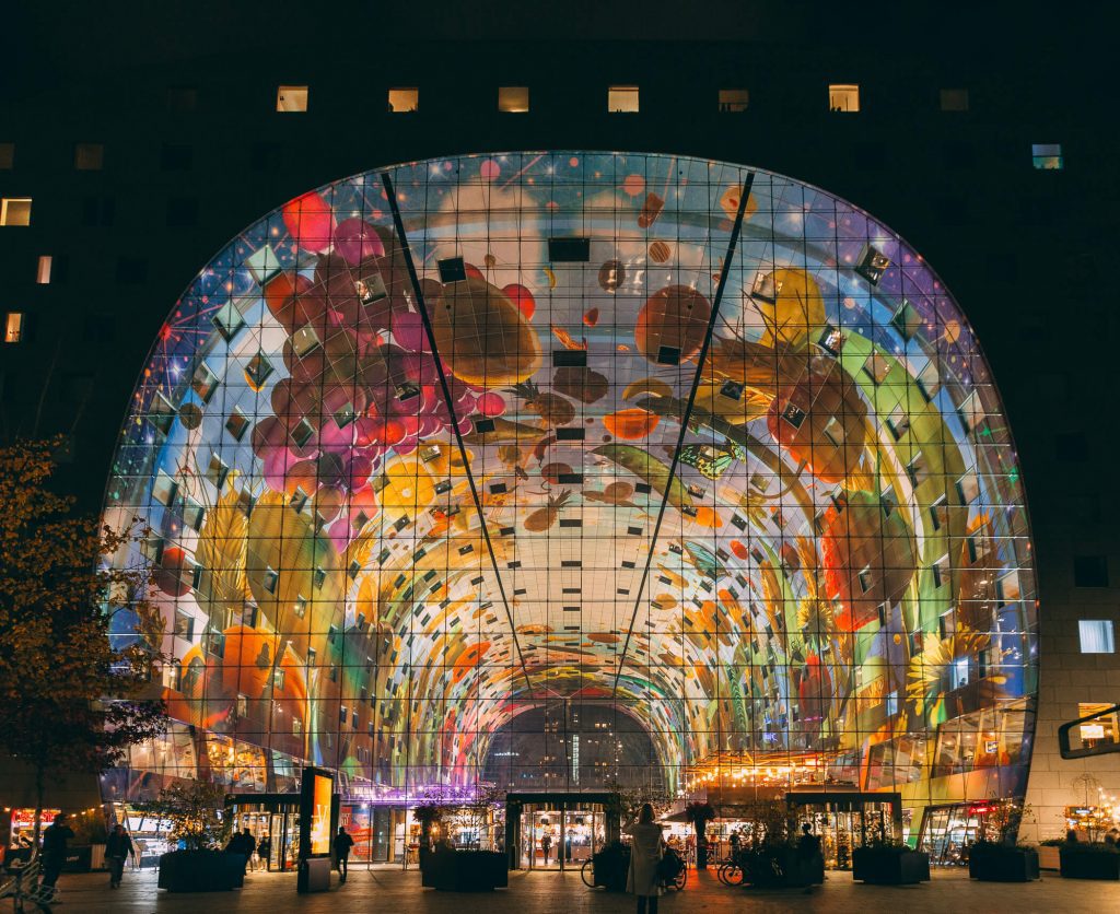 An illuminated De Markthal at night, showing off the amazing ceiling artwork - Rotterdam, Netherlands