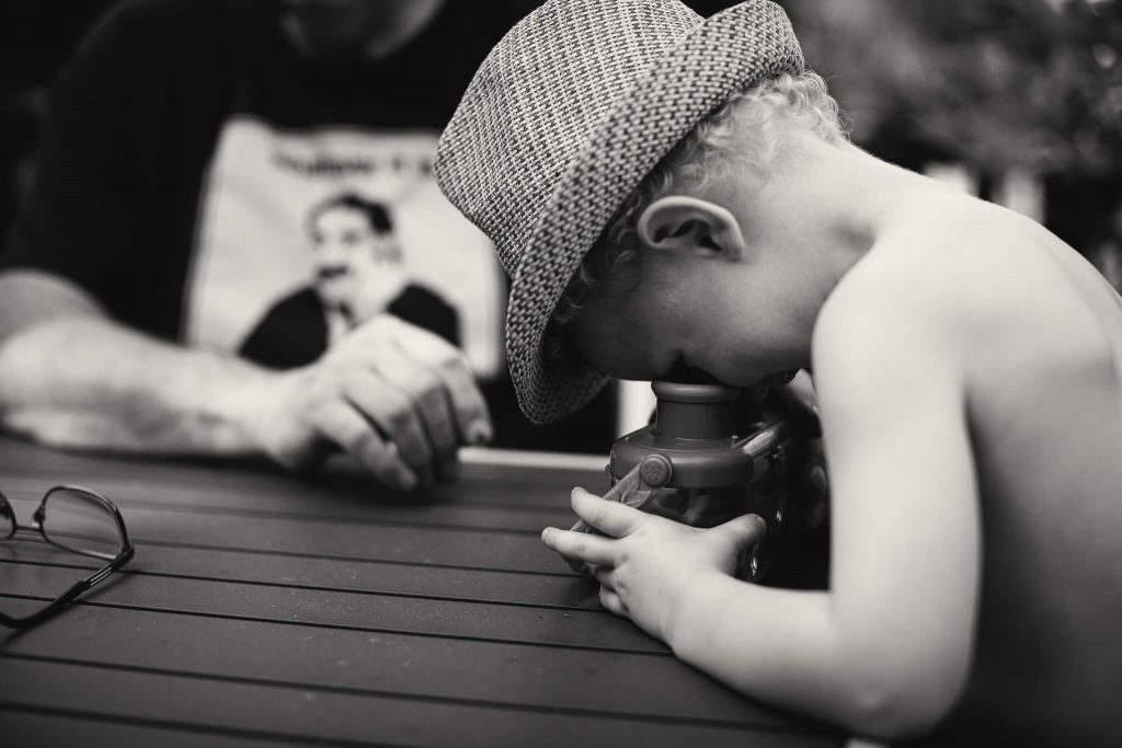 Black & white photo of a young boy looking at a bug in a magnifier