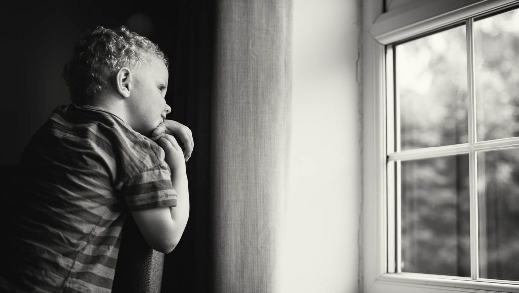 Natural light photography of a boy looking out of a window