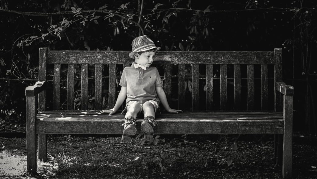 Black and white photograph of a young boy sat on a bench