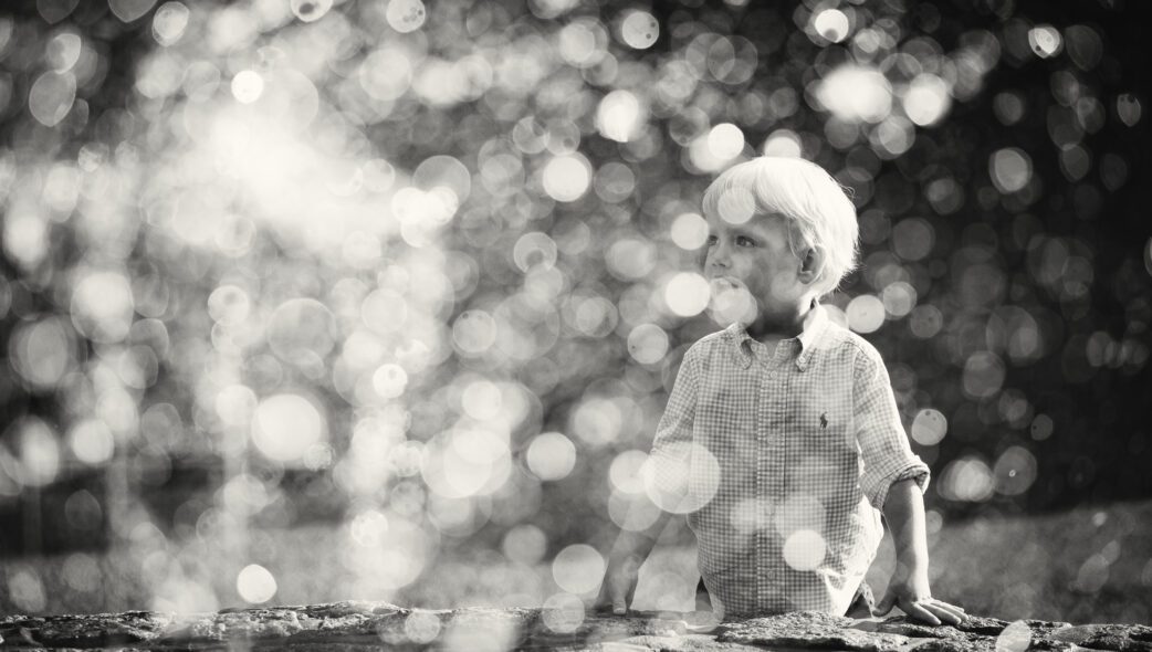Black and white portrait of a young boy playing by a fountain, shot through the water