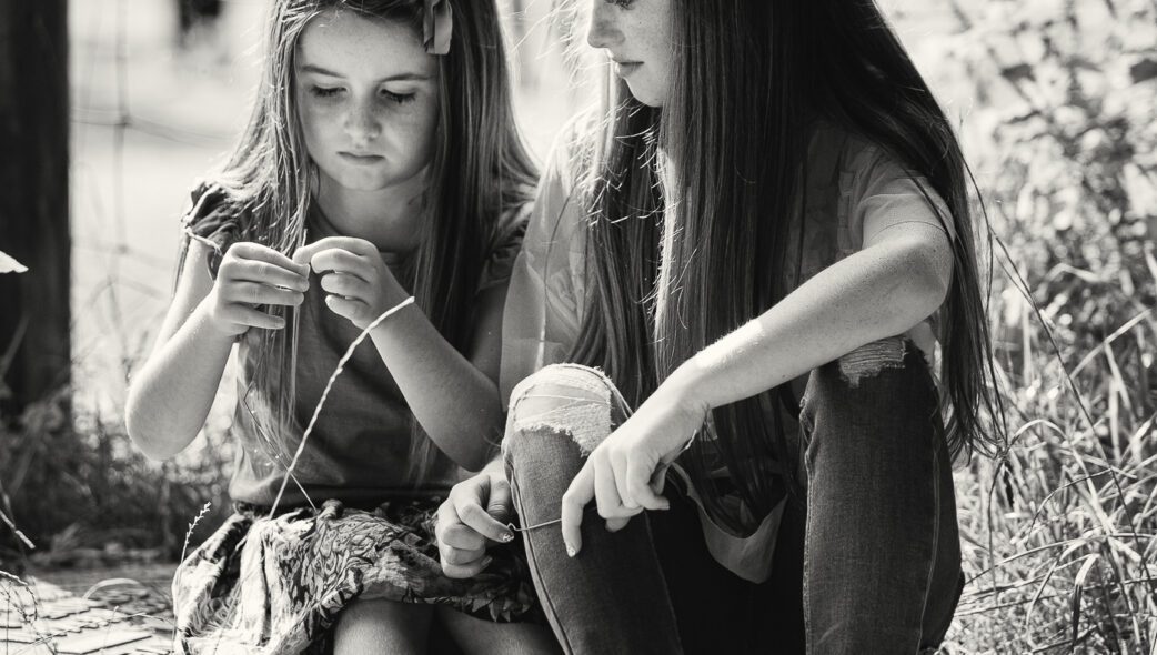Fine art black and white photo of two sisters sitting in the sun