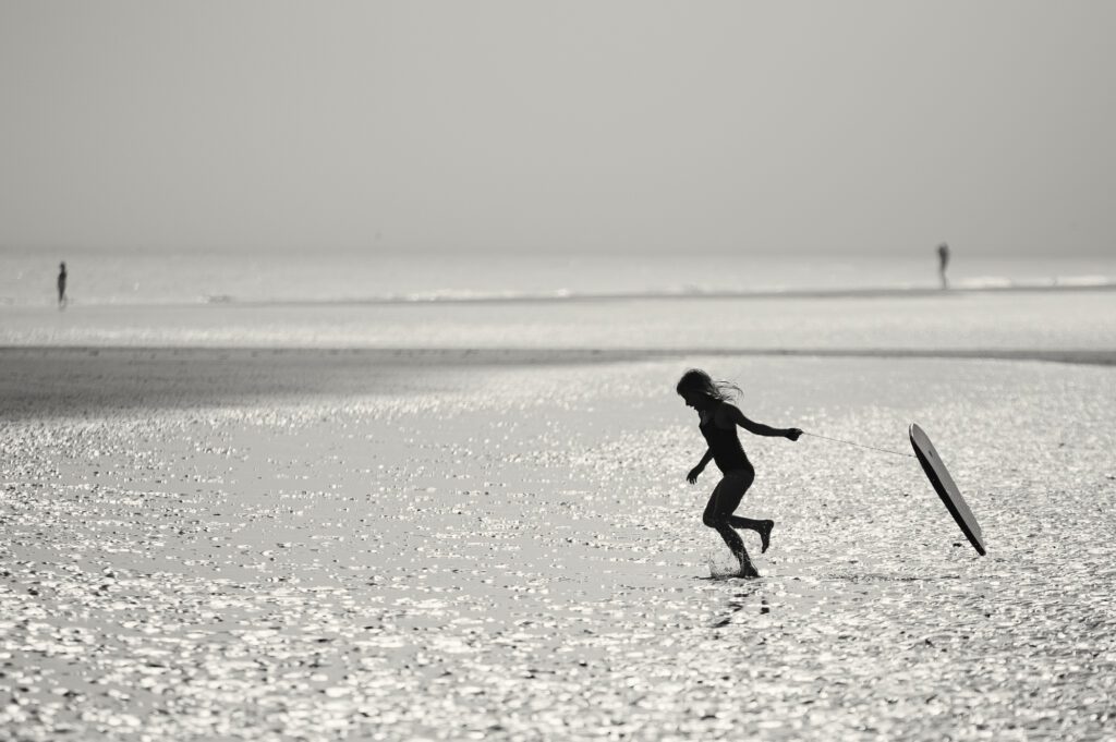 Silhouette of a young girl running into the sea dragging a body board behind her