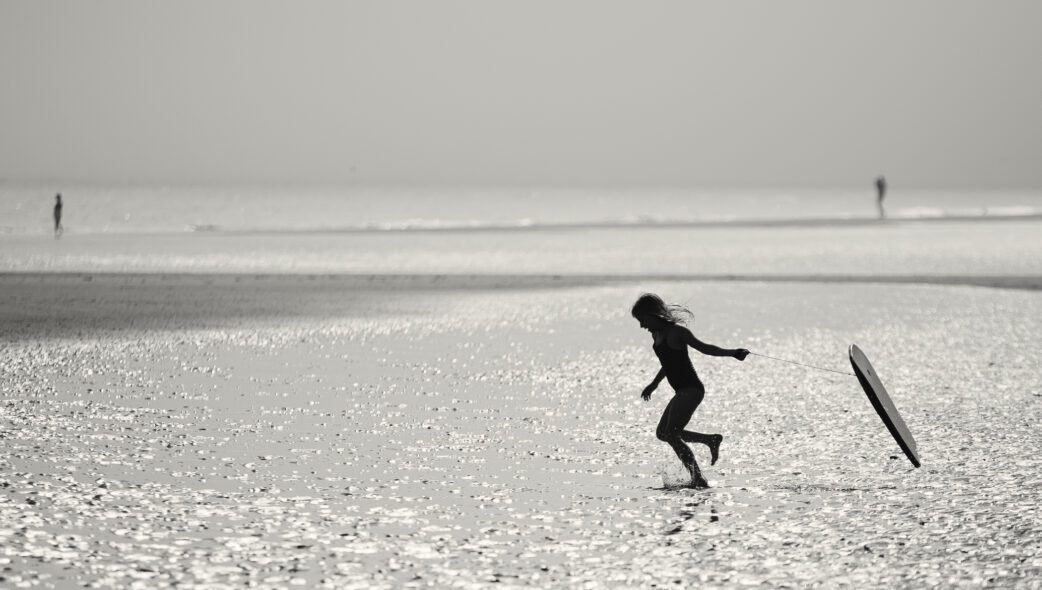 Silhouette of a young girl running into the sea dragging a body board behind her