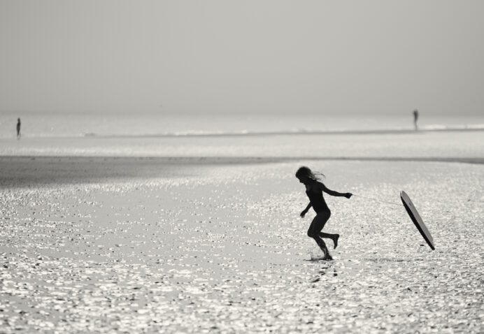 Silhouette of a young girl running into the sea dragging a body board behind her