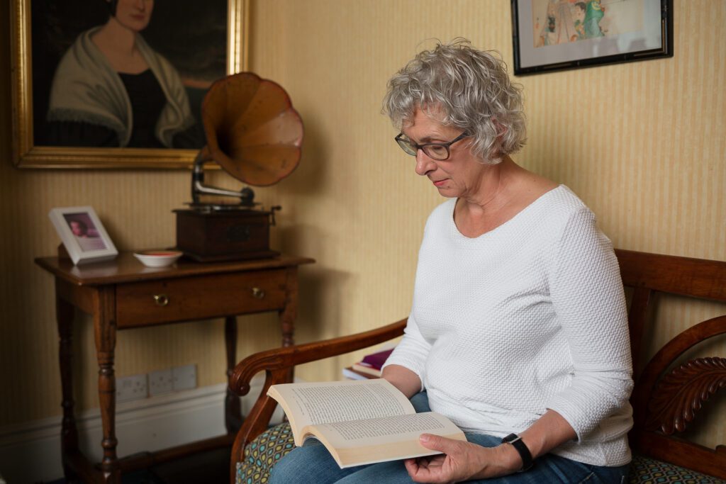 Environmental portrait of a woman sat reading a book in a living room with gramaphone in the background