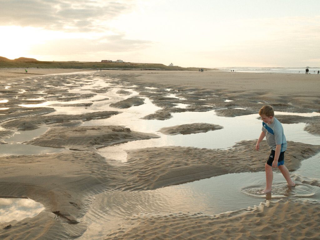 Playing in the shallow pool of Bamburgh Beach, Northumberland at sunset